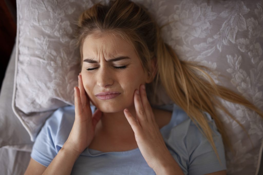 Woman waking with TMJ pain from bruxism or teeth grinding in sleep